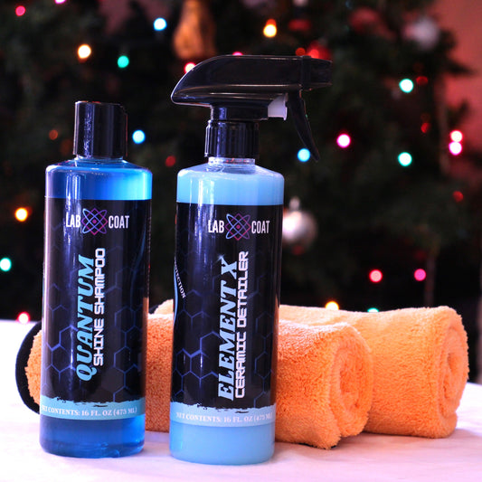 Two bottles of car care products and a microfiber towel on a table with a Christmas tree in the background.